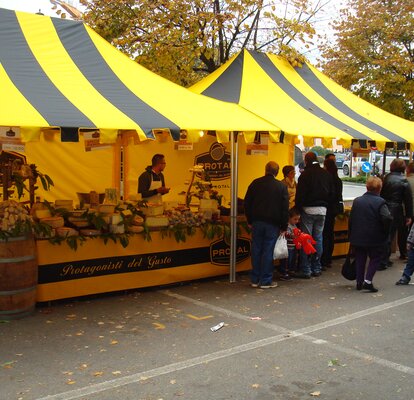 Coppia di gazebo pieghevoli 4,5x3m per la vendita di formaggi di Protal. Tetto con tettoia giallo e nero e frontalino personalizzato su misura a frange. 