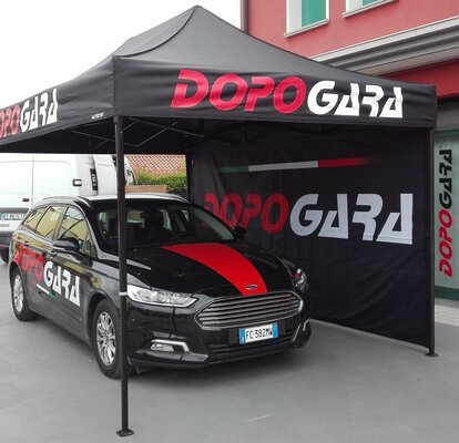 Gazebo pieghevole 4,5x3 m nero con una parete laterale intera personalizzato con stampa logo utilizzato da DopoGara come gazebo promozionale per auto. 