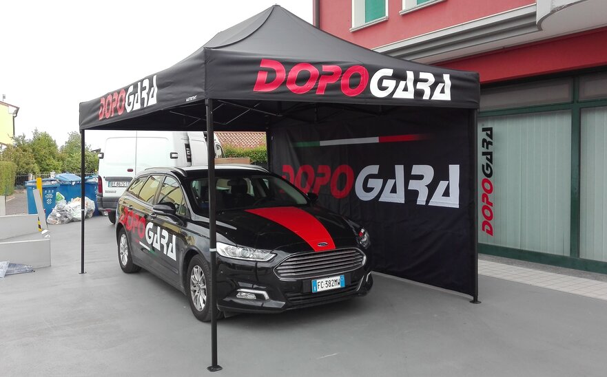 Gazebo pieghevole 4,5x3 m nero con una parete laterale intera personalizzato con stampa logo utilizzato da DopoGara come gazebo promozionale per auto. 