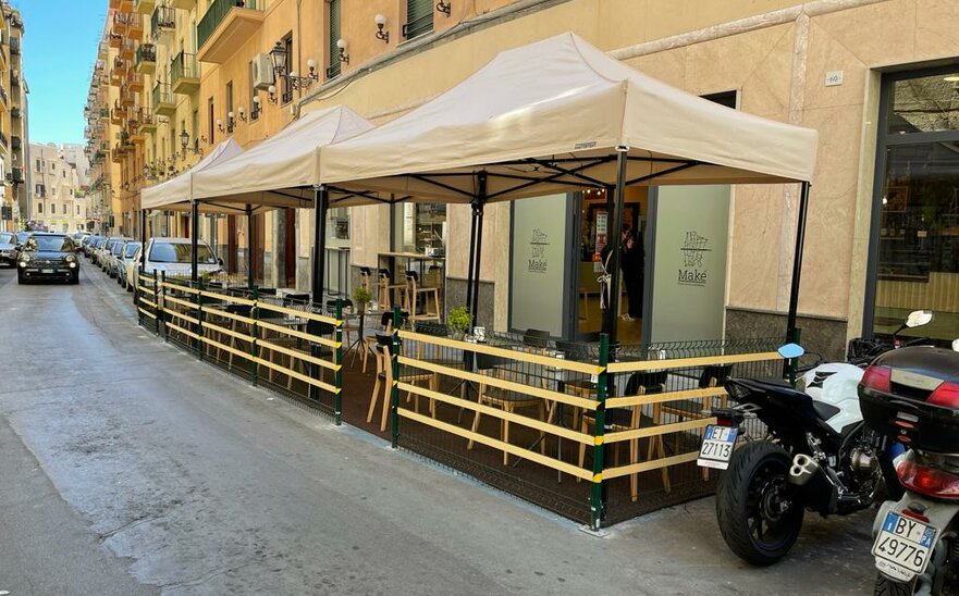 Gazebo pieghevole elegante e moderno beige 4x2 m con struttura in alluminio nera. Fila di gazebo utilizzati nell'area esterna del locale bar ristorante Maké per le vie della città