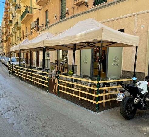 Elegant and modern beige folding gazebo 4x2 m with black aluminium frame. Row of gazebos used in the outdoor area of the local bar and restaurant Maké on the city streets
