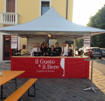 Gazebo pieghevole 4x4 m bianco con struttura rossa e pareti laterali a mezza altezza rosse con logo "il gusto del bere" e con bancone  per servizio vino a evento all'aperto. 