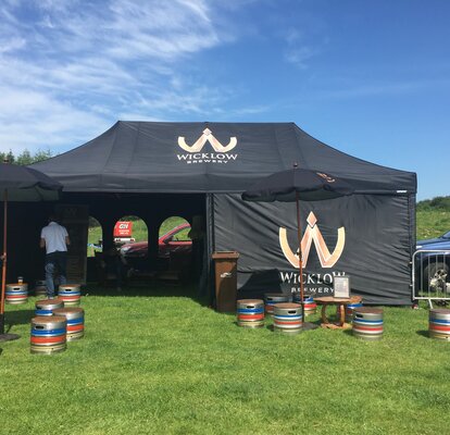 Gazebo pieghevole nero 8x4m con pareti laterali con finestre e logo Wicklow Brewery per evento all'aperto.