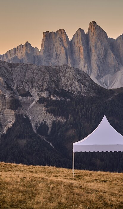 The white pagoda tent stands on the mountain. Behind it stretches a dreamlike mountain range in the sunset.