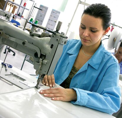 A woman is sewing the fabrics of the gazebo together. She is sitting by the sewing machine.