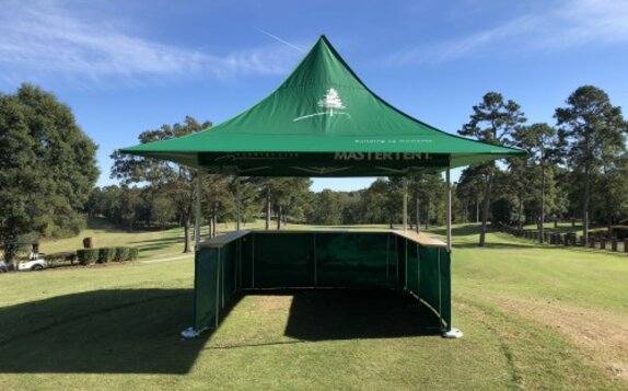 Ein grünes Faltzelt mit Theke an drei Seiten und Vordächern steht auf einem Golfplatz. 