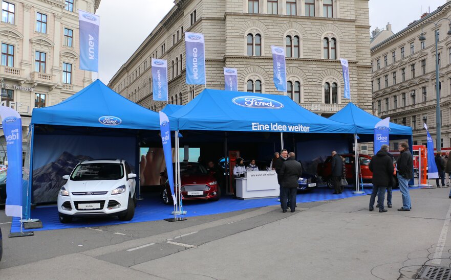 Jasnoniebieski namiot promocyjny 8x4 m Ford z nadrukiem logo, napisów i flag oraz jasnoniebieski namiot promocyjny 3x3 m ze ścianą boczną