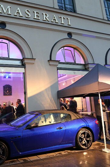 A sales stand 3x3 m with black roof in front of the building. Next to the folding pavilion a blue Maserati.