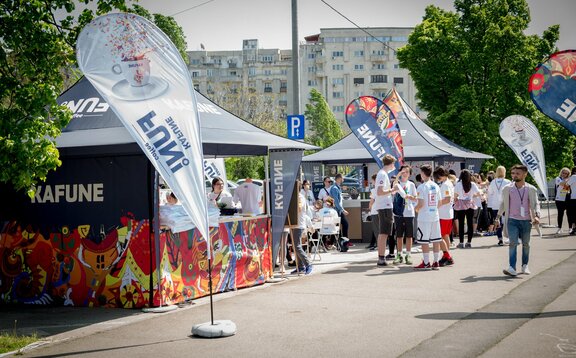 Faltpavillon 3x3 m mit individuellem Aufdruck und Kafune-Logo mit vollen Seitenwänden, halbhohen Seitenwänden mit Theke und individuellen Fahnen. Die Pavillons werden mit 28 kg Gewichten am Boden befestigt.