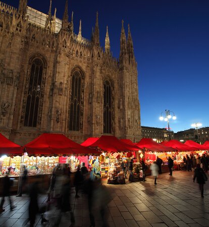 Serie di gazebo rossi di Natale 6x4m con frontalino ondulato, pareti laterali chiuse e a mezza altezza con decorazioni natalizie utilizzati ai mercatini di Natale in Piazza Duomo a Milano di sera - Mastertent