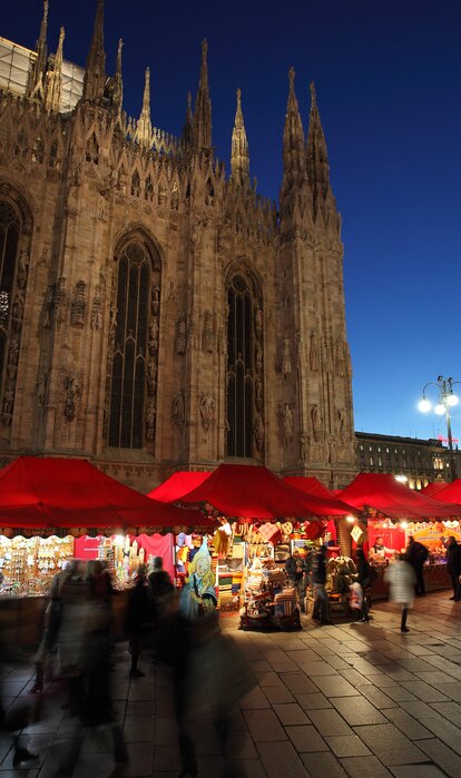 Serie di gazebo rossi di Natale 6x4m con frontalino ondulato, pareti laterali chiuse e a mezza altezza con decorazioni natalizie utilizzati ai mercatini di Natale in Piazza Duomo a Milano di sera - Mastertent