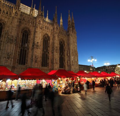 Serie di gazebo rossi di Natale 6x4m con frontalino ondulato, pareti laterali chiuse e a mezza altezza con decorazioni natalizie utilizzati ai mercatini di Natale in Piazza Duomo a Milano di sera - Mastertent