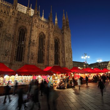 Serie di gazebo rossi di Natale 6x4m con frontalino ondulato, pareti laterali chiuse e a mezza altezza con decorazioni natalizie utilizzati ai mercatini di Natale in Piazza Duomo a Milano di sera - Mastertent