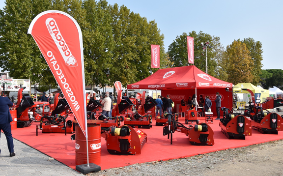 The red gazebo by Ceccato stands in the middle of red machines. Underneath is a red carpet. The exhibition and fair tent has 2 flags on the roof. Another advertising flag is in the front.