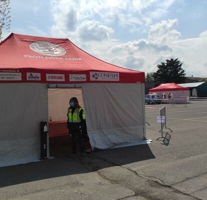 Su un parcheggio ci sono due gazebo Rescue con pareti laterali bianche e tetti rossi. In più ci sono due gazebo verdi e un'impiegata in uno dei gazebo Rescue..