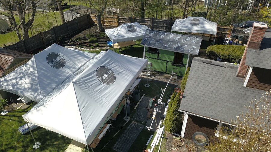 In un giardino vicino a una casa ci sono quattro gazebo pieghevoli con dimensioni differenti.