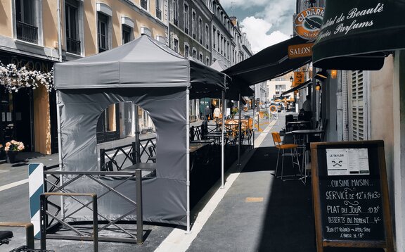 In a street in front of a bar are two black folding gazebos with a sidewall with a round-arched windows.