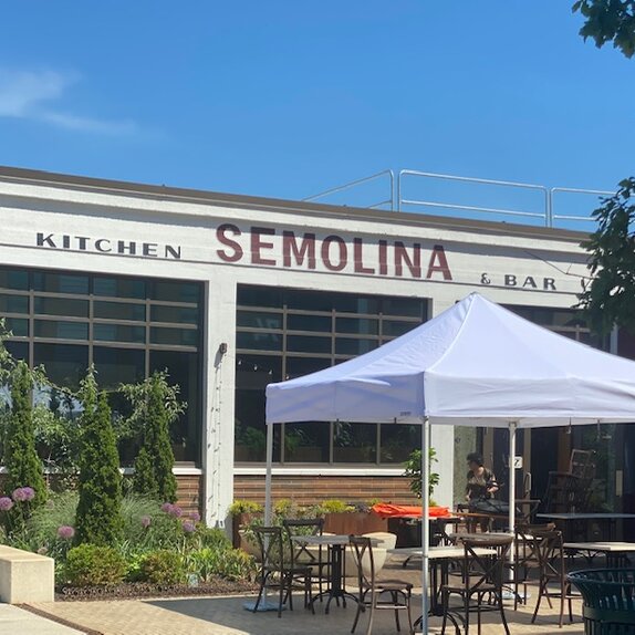 Auf der Terrasse eines Restaurants steht ein weißer Faltpavillon. Darunter befinden sich Tische und Stühle.