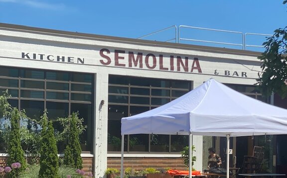 Auf der Terrasse eines Restaurants steht ein weißer Faltpavillon. Darunter befinden sich Tische und Stühle.