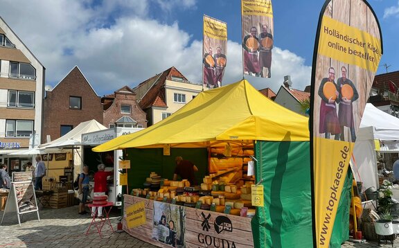 The 4.5x3 m yellow market gazebo has a green canopy and side walls. Customised flags to increase visibility and half a wall fully sublimation-printed