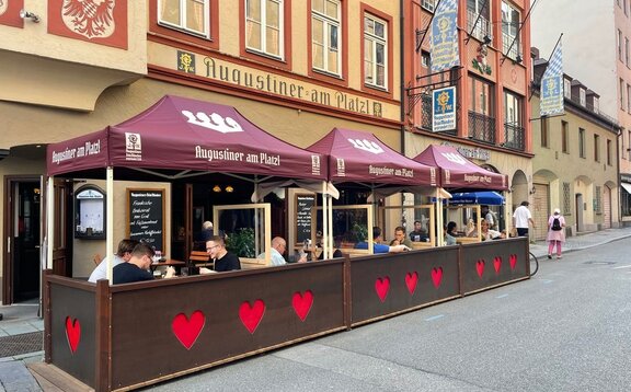 Neben einer Straße vor einem Restaurant stehen drei Faltzelte mit rotem Dach. Unter dem Zelt stehen Tische und Stühle