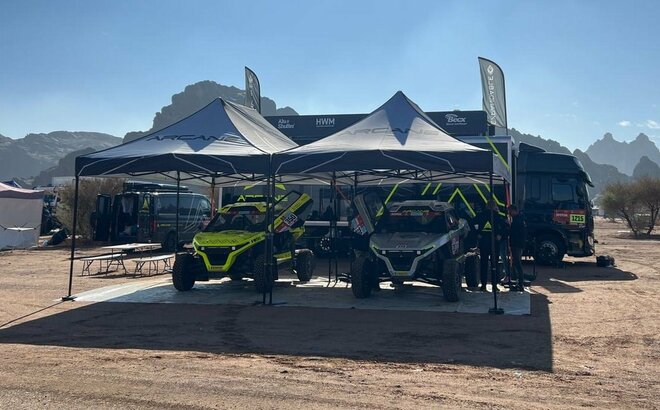 due gazebi da gara neri e bianchi al rally Dakar 2022 con furgone nero Arcane vicino alle montagne sulla sabbia