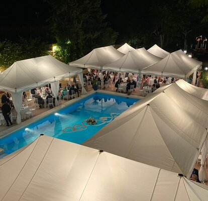 Eleganti gazebo da matrimonio in bianco si trovano vicino alla piscina. Sotto di essi ci sono tante persone sedute ai tavoli. 