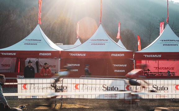 Auf dem Bild sind drei Faltpavillons mit roter Dachflagge des Mountainbike-Teams Thömus Maxon zu sehen. Sie haben weiße Dächer und rote Seitenwände. Im Hintergrund sieht man noch drei weitere Dachspitzen mit den Flaggen.