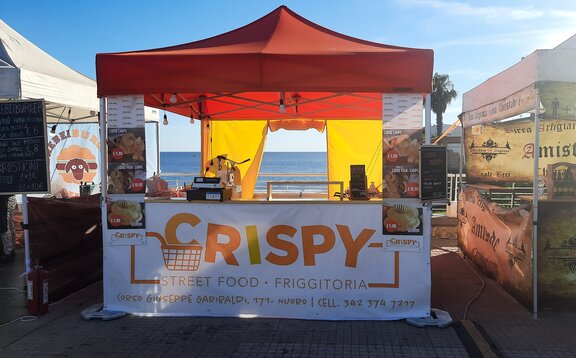 The picture shows a 3x3 m folding gazebo used as a street food vending tent. It has an orange roof, a counter, a sidewall with a door, and is personalized with a promotional print.