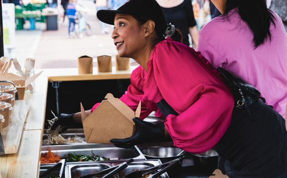 Auf dem Bild ist ein schwarzer 3x3 m Faltpavillon, bedruckt mit dem Logo von Pad Thai. Der Faltpavillon hat eine Seitenwand mit Tür und eine halbhohe Seitenwand mit Theke, wo das Essen serviert wird.