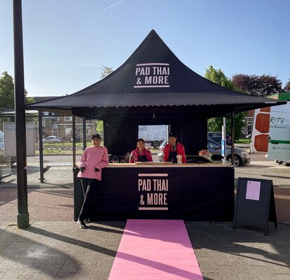 A black 10x10 4-awning canopy tent with counters set up for cooking and vending Thai food.