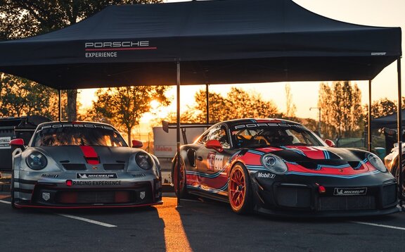 2 Porsche Experience Racing Modelle nebeneinander unter einem schwarzen 6x3 Oxford Faltpavillon mit gerader Blende und schwarzem Alugestell im Hintergrund Sonnenuntergang