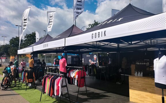 Mehrere schwarz-weiße Faltpavillons mit stehen nebeneinander bei einem Event. Alle haben eine personalisierte Dachflagge.