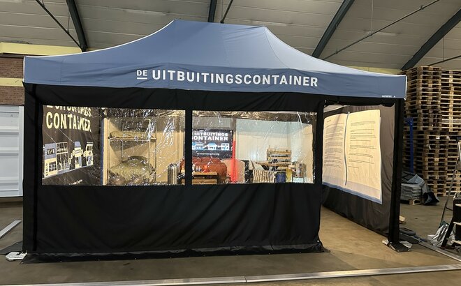 You can see a blue 6x4 m folding gazebo. It has two large windows at the front and a door through which you can see into the tent. You can see that the tent is printed on the inside of the right and left side walls. It also has a white logo on the roof.