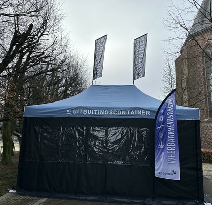 Je ziet een blauwe easy up tent 6x4 m. Het heeft twee grote ramen aan de voorkant. Het heeft ook twee vlaggen op het dak en één voor de tent. Op het dak en de vlaggen is een wit logo te zien.