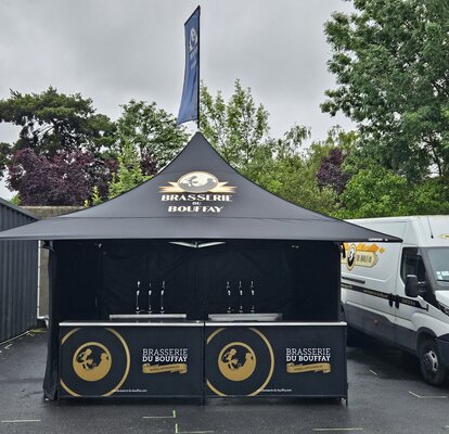 L'immagine mostra un gazebo pieghevole nero di 3x3 m con una stampa personalizzata sulle pareti laterali, sul tetto e sulla bandiera del tetto. Il gazebo è dotato anche di quattro tettoie.