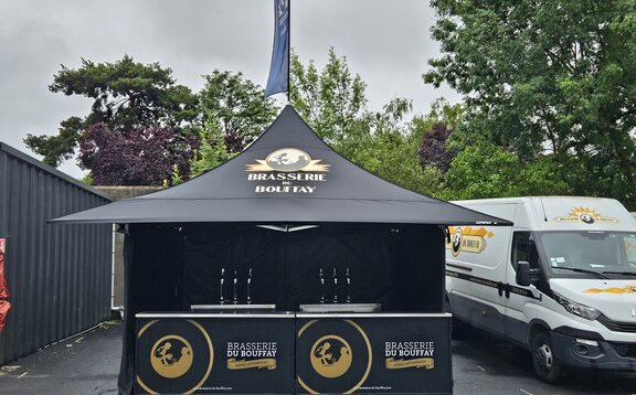 The picture shows a black 3x3 m folding gazebo with a personalised print on the sidewalls, roof and roof flag. The gazebo also has four awnings.