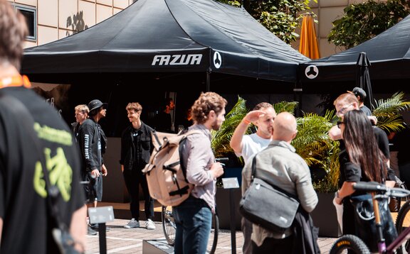 You can see a black 8x4 m gazebo with three roof flags. The flags and the roof of the gazebo are printed with the customer's white logo. Many people can be seen in the foreground.