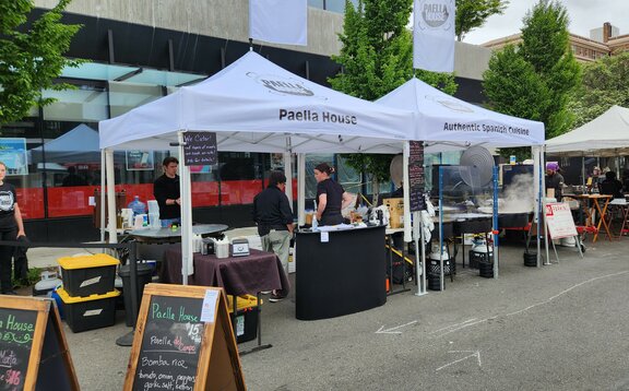 Two white folding gazebos stand at a market. They both have printed roofs and one printed flag each.