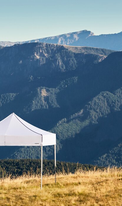 White gazebos on the Plose mountain. In the background there is a mountain range called Dolomites. 