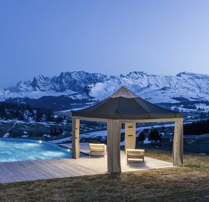 Il gazebo pieghevole Loden è posizionato sulla terrazza vicino la piscina. Nello sfondo le montagne vengono illuminate dalla luna.