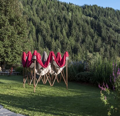 Leicht aufgezogener Faltpavillon mit rot-grauem Lodenstoff-Überzug im Garten.