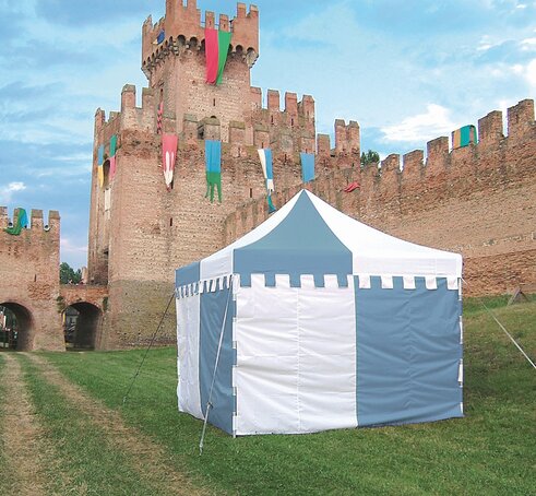A custom made gazebo in the colours blue and white is standing in the meadow in front of a castle. The valance of the roof reminds at a castle. 