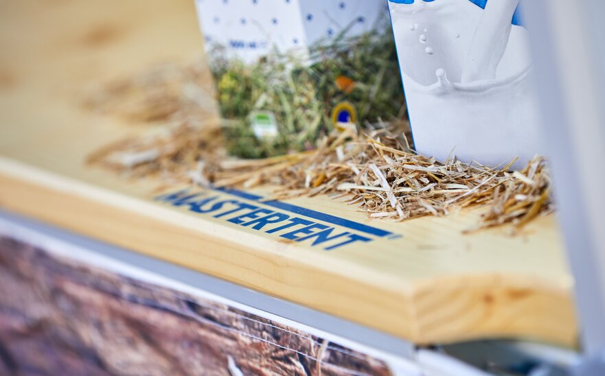 Detailansicht der Holztheke von MASTERTENT. Darauf liegt Stroh und es steht eine Milchpackung drauf.