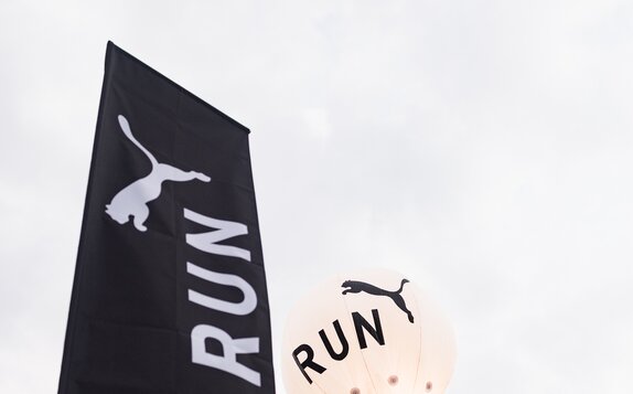 A black peak flag printed with a white Puma logo on top of a Mastertent canopy tent.